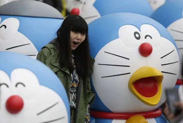 A visitor poses for a photo next to a Doraemon model during an exhibition in Beijing April 19, 2014. The exhibition, which showcased a hundred models of the Japanese cartoon character in different poses and expressions, will run from April 19 to June 22. (Photo by Jason Lee/Reuters)