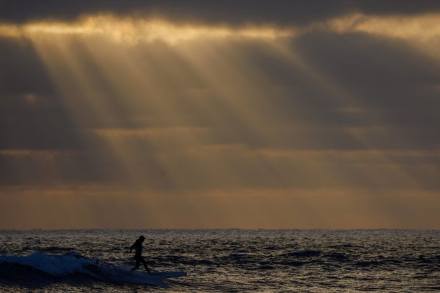 A lone surfer catches a wave as the sun sets into a bank of clouds at Cardiff State Beach in Encinitas, California on July 2, 2024. (Photo by Mike Bake/Reuters)