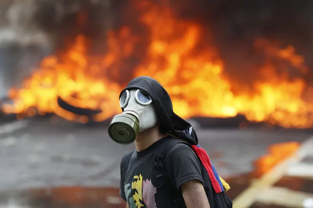 An anti-government protester stands in front of burning barricade on a highway in Caracas, Venezuela, Monday, April 24, 2017. (Photo by Ariana Cubillos/AP Photo)
