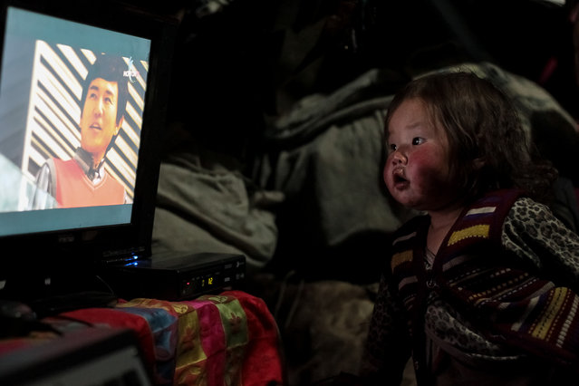 A girl watches TV in Nalaikh, Mongolia onMay 13, 2016, while her father leaves to spend the night foraging through abandoned mining sites hoping to find jade, gold and other valuable minerals to sell. (Photo by Asher Svidensky/Barcroft Images)