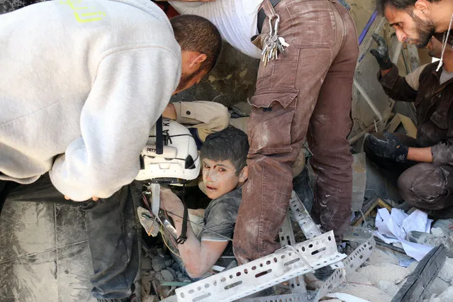 Syrian civil defence volunteers help a boy out of the rubble following a reported attack by Syrian government forces on May 30, 2016, in the Tariq al-Bab neighbourhood in the northern city of Aleppo. (Photo by Ameer Alhalbi/AFP Photo)