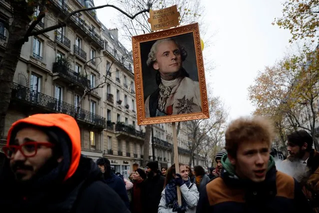 A woman holds a portrait of French President Emmanuel Macron painted as a royalty with a sign on top of it reading “14 mai 2017 restoration of the monarchy” during a demonstration against the pension overhauls, in Paris, on December 5, 2019 as part of a nationwide strike. Trains cancelled, schools closed: France scrambled to make contingency plans on for a huge strike against pension overhauls that poses one of the biggest challenges yet to French President's sweeping reform drive. (Photo by Thomas Samson/AFP Photo)