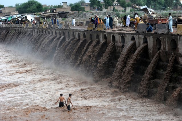 People wade through a flooded bridge on a stream, which is overflowing following heavy rains, in Khyber, Peshawar, Pakistan, on August 04, 2024. Lightnings and heavy rains killed dozens of people, mostly farmers, across Pakistan in the past three days, officials said Monday, as authorities declared a state of emergency in the country's southwest following an overnight rainfall to avoid any further casualties and damages. (Photo by Hussain Ali/Anadolu via Getty Images)