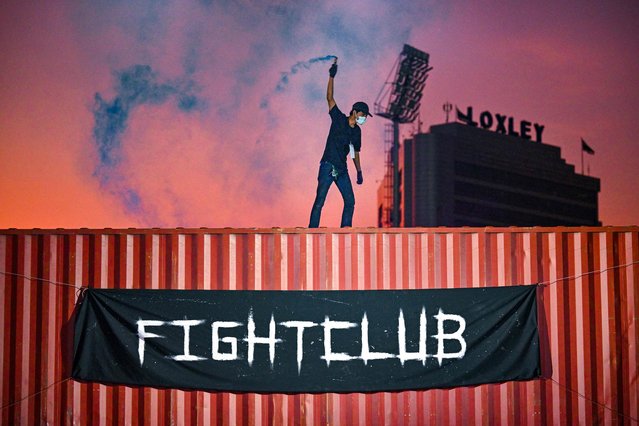 This photo taken on April 16, 2022 shows a man lighting a flare on top of a shipping container at an event by Fight Club Thailand, an underground organisation that hosts unsanctioned fights of various martial arts disciplines, in a parking lot in the Klong Toey district of Bangkok. (Photo by Lillian Suwanrumpha/AFP Photo)