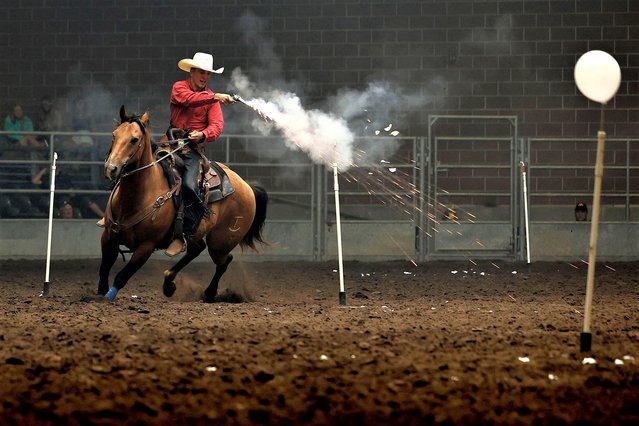 A rider blasts balloons with blanks as he competes in the Cowboy Mounted Shooting event in the Exhibition Center at the Iowa State Fair on August 11, 2023 in Des Moines, Iowa. Contestants are timed as they gallop their horses at high speed through a patterned course of gates while shooting blank rounds, popping balloons at a range of 20 feet or less. (Photo by Chip Somodevilla/Getty Images)