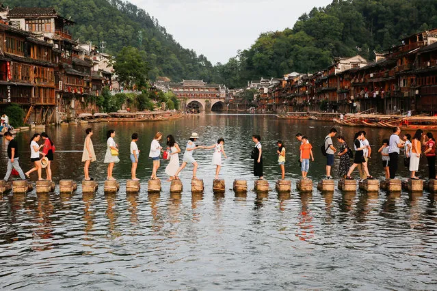 This photo taken on August 5, 2017 shows visitors walking on stone piers crossing the Tuojiang River in the ancient town of Fenghuang in Xiangxi, in China' s central Hunan province. The old town district of Fenghuang nestles on the banks of a winding river in a picturesque, mountainous part of Hunan province, and boasts stunning Qing and Ming dynasty architecture dating back hundreds of years. (Photo by AFP Photo/Stringer)
