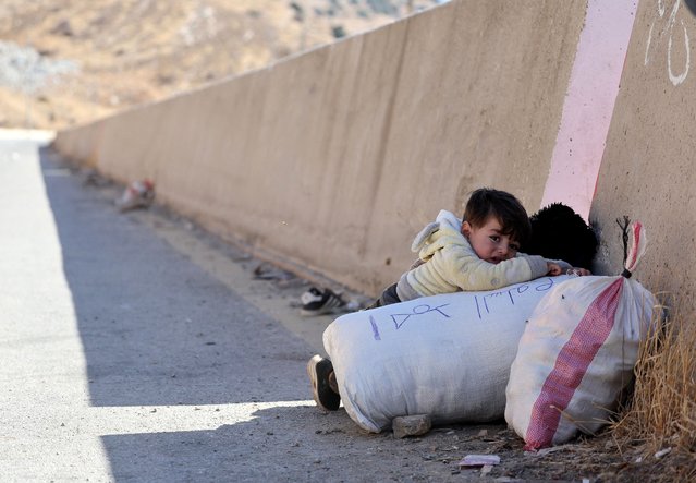 A child holds onto their belongings while crossing from Lebanon into Syria, as people flee the ongoing hostilities between Hezbollah and Israeli forces, at Masnaa border crossing, Lebanon on October 28, 2024. (Photo by Mohamed Abd El Ghany/Reuters)