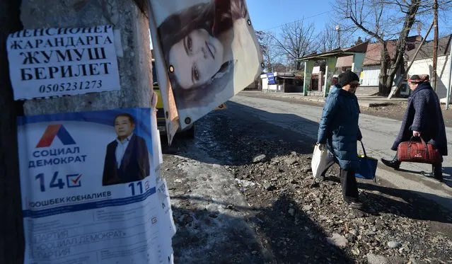 Women walk along a street near a campaign poster of a candidate in the upcoming parliamentary election in the village of Tash-Dobo, some 25km from Bishkek, on November 24, 2021. (Photo by Vyacheslav Oseledko/AFP Photo)