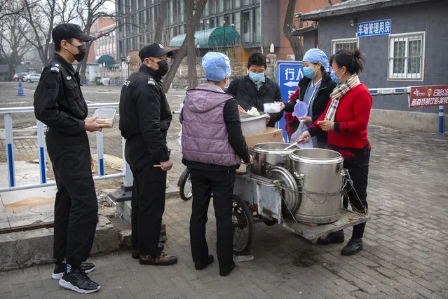 Security guards line up as workers in face masks dispense lunch outside of an office building in Beijing, Friday, February 21, 2020. China reported a further fall in new virus cases to 889 on Friday as health officials expressed optimism over containment of the outbreak that has caused more than 2,200 deaths and is spreading elsewhere. (Photo by Mark Schiefelbein/AP Photo)