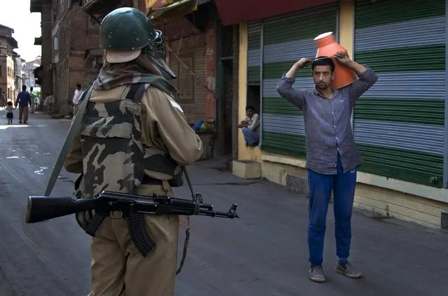 Indian paramilitary soldier questions a Kashmiri man selling milk before turning him back near a temporary checkpoint during curfew in Srinagar, Indian controlled Kashmir, Friday, July 29, 2016. Authorities have re-imposed a curfew in the main city of Srinagar in Indian-controlled Kashmir to prevent a protest march to the main mosque called by separatist leaders before Friday afternoon prayers. (Photo by Dar Yasin/AP Photo)