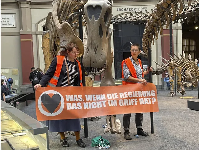Two climate activists carrying a banner “What if the government can't handle it?” have stuck themselves to the handrails of a dinosaur at Berlin's Museum of Natural History in Berlin, Germany, Sunday, October 30, 2022. Commenting on the action, the “Last Generation” protest group said, “Just as the dinosaurs did back then, we are threatened with climate changes that we will not be able to withstand. If we don't want to face extinction, we must act now”. (Photo by Paul Zinken/dpa via AP Photo)