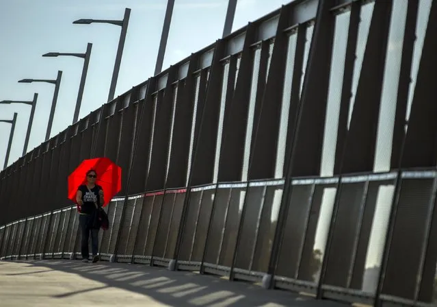 A woman uses an umbrella to sheld herself from the sun as she crosses the highway on a pedestrian bridge in the border town of San Ysidro, California September 2, 2015. Picture taken September 2, 2015. (Photo by Mike Blake/Reuters)
