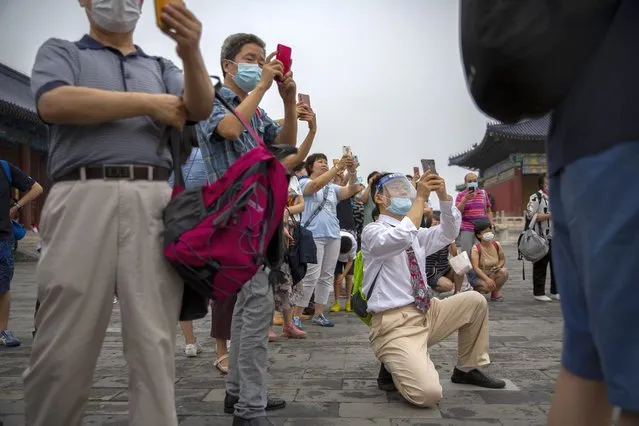 Parents wearing face masks to protect against the coronavirus take photos of students as they pose for a group photo at the Temple of Heaven in Beijing, Saturday, July 18, 2020. Authorities in a city in far western China have reduced subways, buses and taxis and closed off some residential communities amid a new coronavirus outbreak, according to Chinese media reports. They also placed restrictions on people leaving the city, including a suspension of subway service to the airport. (Photo by Mark Schiefelbein/AP Photo)