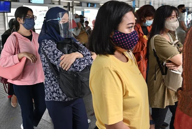 People wearing face masks as a preventive measure against the COVID-19 coronavirus queue to get on a bus in Jakarta on August 13, 2020. (Photo by Adek Berry/AFP Photo)