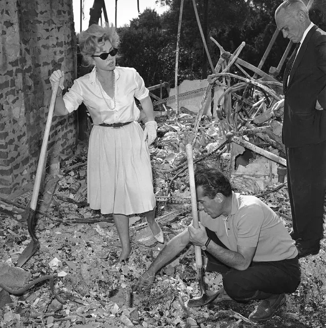 In this November 8, 1961 file photo, Zsa Zsa Gabor, aided by a friend, Robert Straile, digs through the ashes of her $275,000 Bel-Air home in Los Angeles. Nearly 500 homes burned in the area during the infamous Bel Air Fire of 1961. Celebrities, including Burt Lancaster and Zsa Zsa Gabor, lost homes in the fire. (Photo by Dick Strobel/AP Photo)