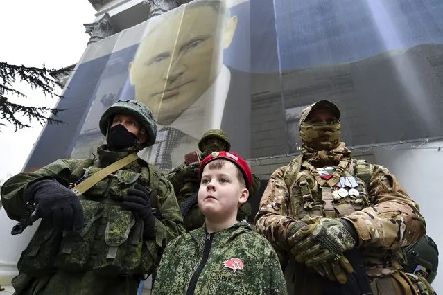A boy and Russian soldiers take part in an action to mark the ninth anniversary of the Crimea annexation from Ukraine, in Yalta, Crimea, Friday, March 17, 2023. (Photo by AP Photo/Stringer)