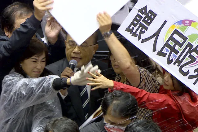 In this image made from video, Taiwanese Premier Su Tseng-chang holds a microphone as opposition party lawmakers from the Nationalist party (KMT) block his attempt to speak during a parliament session in Taipei, Taiwan, Friday, November 27, 2020. Taiwan's lawmakers got into a fist fight and threw pig guts at each other Friday over a soon-to-be enacted policy that would allow imports of U.S. pork and beef. The banner at right reads: “Democratic Progressive Party feeds people with ractopamine pork”. (Photo by FTV via AP Photo)