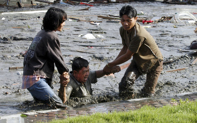 In this December 26, 2004 file photo, Acehnese youths try to pull a man to higher ground through a flooded street a moment after tsunami strike in the provincial capital of Banda Aceh, Aceh province, Indonesia. (Photo by Bedu Saini/AP Photo/Serambi Indonesia)