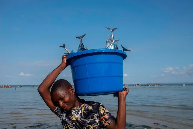 A fisherman balances a bucket of fishes on his shoulder on December 9, 2020 outside on the coast of the Paquitequete district of Pemba where internal displaced people are fleeing from unrest in the norther part of the Cabo Delgado area in Mozambique. (Photo by Alfredo Zuniga/AFP Photo)