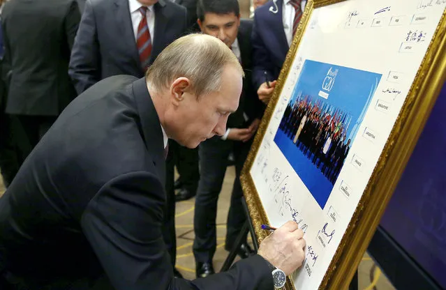 Russian President Vladimir Putin signs a print of the G20-Turkey family photo at the Group of 20 (G20) summit, in the Mediterranean resort city of Antalya, on November 15, 2015. World leaders raised the alarm over an escalating international movement of "foreign terrorist fighters" in a draft statement drawn up at a summit in Turkey after the Paris assaults claimed by Islamic State jihadists. (Photo by Kayhan Ozer/AFP Photo)