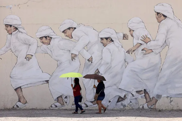 Women walk past a mural painting of Emirati children in one of Dubai's markets on April 15, 2023 during the last week of the Muslim fasting month of Ramadan. (Photo by Karim Sahib/AFP Photo)