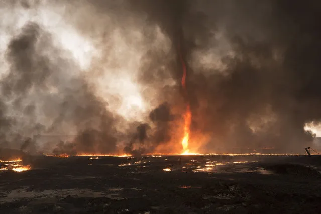 Smoke and a flaming tornado are seen at a burning oil facility on November 8, 2016 in the town of Qayyarah, Iraq. Oil wells in and around the town of Qayyarah, Iraq, we set alight in July 2016 by Islamic State extremists as the Iraqi military began an offensive to liberated the town .For two months the residents of the town have lived under an almost constant smoke cloud, the only respite coming when the wind changes. (Photo by Matt Cetti-Roberts/Zuma Press/Rex Features/Shutterstock)