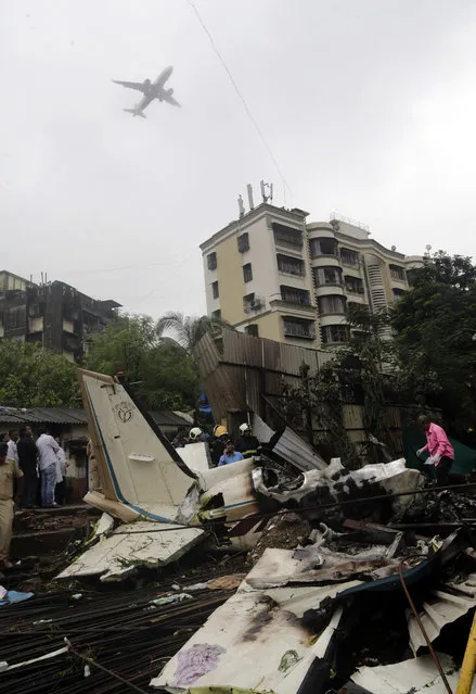 In this Thursday, June 28, 2018, file photo, an aircraft flies above as rescuers stand amid the wreckage of a private chartered plane that crashed in Ghatkopar area, Mumbai, India. The plane hit an open area at a construction site for a multistory building in a crowded area with many residential apartments. At least six people including two on the ground were killed. (Photo by Rajanish Kakade/AP Photo/File)