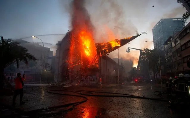 The dome of the church of Asuncion falls down burning in flames after being set on fire by demonstrators on the commemoration of the first anniversary of the social uprising in Chile, in Santiago, on October 18, 2020, as the country prepares for a landmark referendum. (Photo by Claudio Reyes/AFP Photo)