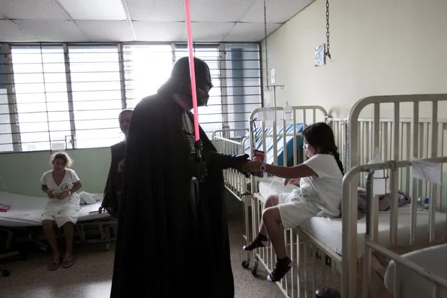 A cosplayer dressed as Darth Vader from the Star Wars movie series interacts with a girl during a charity event organised by the El Salvador Star Wars fan club at the Benjamin Bloom National Children's Hospital in San Salvador, El Salvador December 14, 2015. (Photo by Jose Cabezas/Reuters)