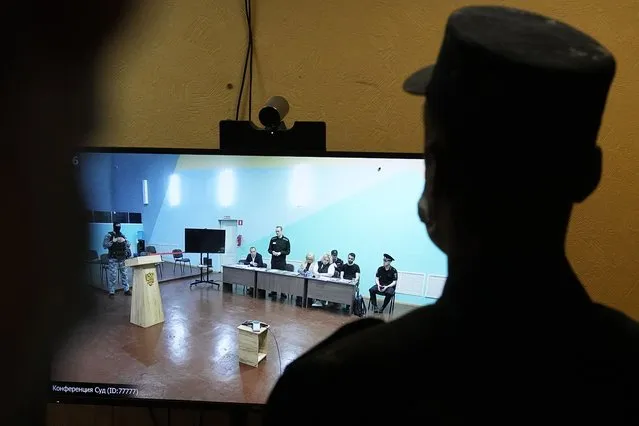 An officer stands in front of a TV screen showing Russian opposition leader Alexei Navalny, standing, speaking between his lawyers in a courtroom, via video link provided by the Russian Federal Penitentiary Service, during a preliminary hearing in the colony, in Melekhovo, Vladimir region, about 260 kilometers (163 miles) northeast of Moscow, Russia, on Monday, June 19, 2023. A Russian court has opened a new trial of imprisoned Russian opposition leader Alexei Navalny that could keep him behind bars for decades. (Photo by Alexander Zemlianichenko/AP Photo)