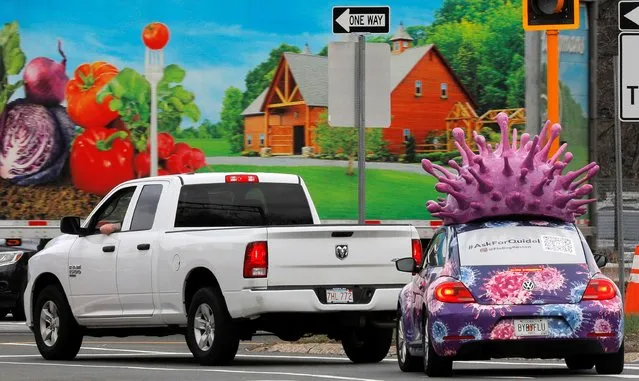 A car, advertising for Quidel Corp., which makes test kits for both the flu and the coronavirus disease (COVID-19), waits at a traffic light with a large model of the influenza virus on its roof, in Medford, Massachusetts, U.S., March 31, 2021. (Photo by Brian Snyder/Reuters)