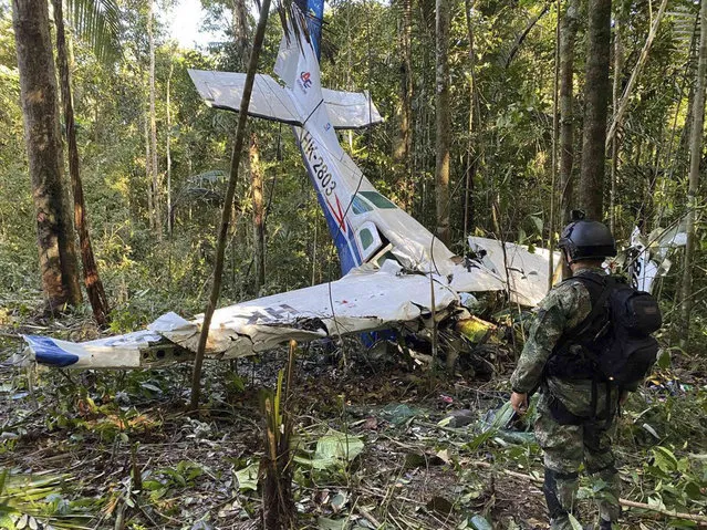 In this photo released by Colombia's Armed Forces Press Office, a soldier stands in front of the wreckage of a Cessna C206, Thursday, May 18, 2023, that crashed in the jungle of Solano in the Caqueta state of Colombia.  A search continues for four Indigenous children who may have survived the deadly plane crash in the Amazon jungle on May 1. On Tuesday, May 16, soldiers found the wreckage and the bodies of three adults, including the pilot and the children's mother. (Photo by Colombia's Armed Forces Press Office via AP Photo)