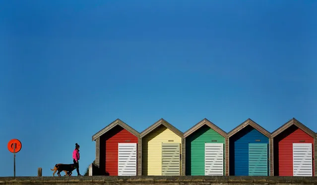 A woman walks her dog past beach huts at Blyth beach in Northumberland in the cold on Wednesday, April 7, 2021. (Photo by Owen Humphreys/PA Images via Getty Images)