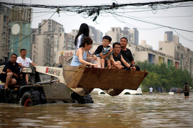People ride on a front loader as they make their way through floodwaters following heavy rainfall in Zhengzhou, Henan province, China on July 23, 2021. (Photo by Aly Song/Reuters)