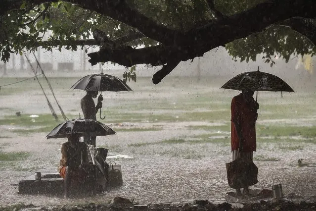 People use umbrellas and take shelter under a tree to keep dry during a heavy monsoon showers in Allahabad on July 20, 2021. (Photo by Sanjay Kanojia/AFP Photo)