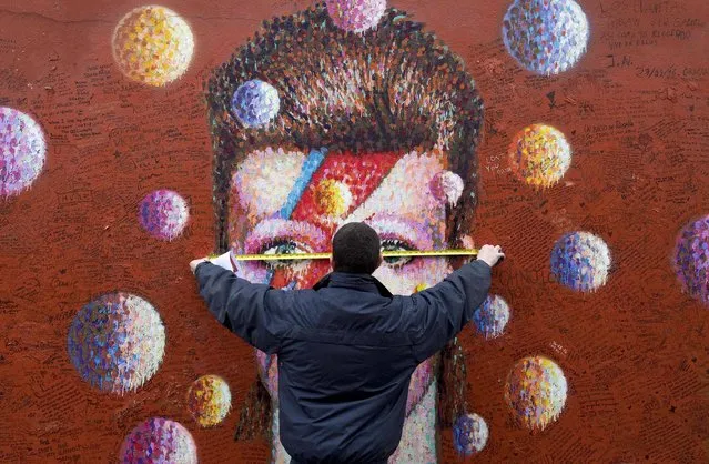 A workman measures up a mural of British musician David Bowie by Australian street artist James Cochran, also known as Jimmy C, in Brixton, south London on January 9, 2017, before mounting an acrylic sheet to protect the art work. January 10, 2017 will mark one year since the death of British rock music legend David Bowie who died of cancer on January 10, 2016 at the age of 69. (Photo by Justin Tallis/AFP Photo)