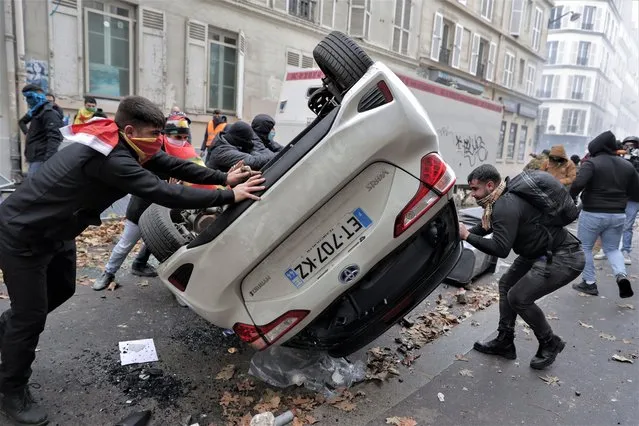 Demonstrators turn a car over during a protest against the recent shooting at the Kurdish culture center in Paris, Saturday, December 24, 2022. Kurdish activists, left-wing politicians and anti-racism groups are holding a protest Saturday in Paris after three people were killed at a Kurdish cultural center in an attack aimed at foreigners. (Photo by Lewis Joly/AP Photo)