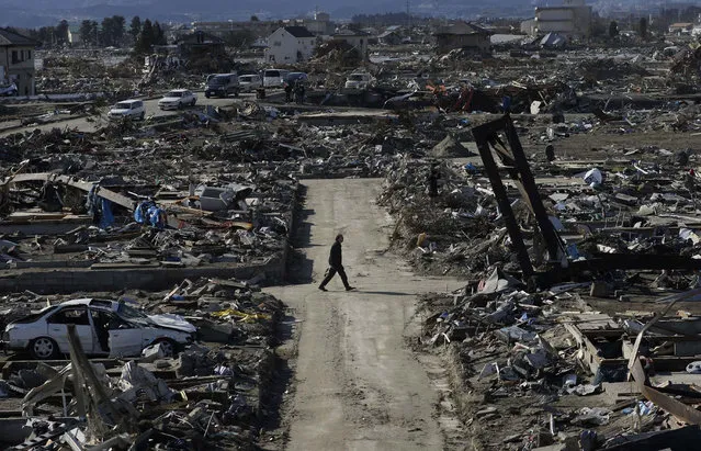 In this March 27, 2011 file photo, a man walks through the destroyed neighborhood below Weather Hill in Natori, Japan. (Photo by Wally Santana/AP Photo)