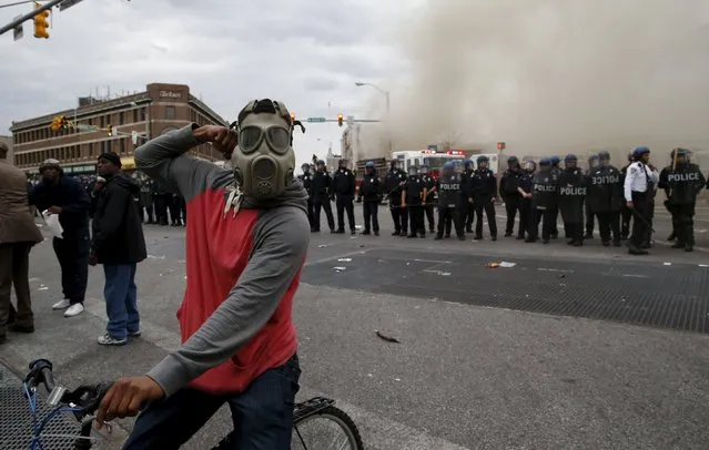 A protestor on a bicycle thrusts his fist in the air next to a line of police, in front of a burning CVS drug store, during clashes in Baltimore, Maryland April 27, 2015. (Photo by Jim Bourg/Reuters)