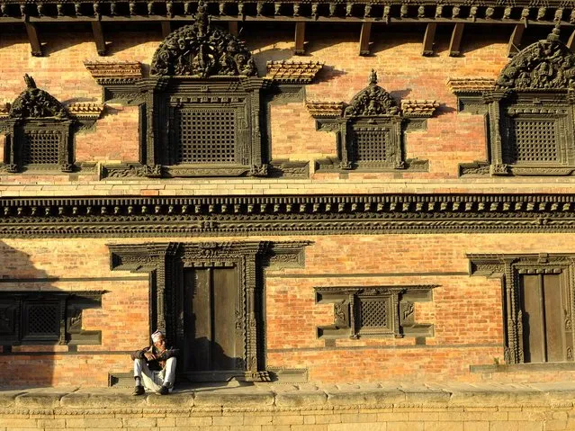 A Nepalese man sits beside intricately carved windows and doors at the Bhaktapur Durbar Square area in Bhaktapur, some 12 kilometres southeast of Kathmandu, on February 6, 2014. Bhaktapur, a UNESCO World Heritage Site, is famous for fine architecture and pottery making, and was once the capital of Nepal during the great Malla Kingdom until the second half of the 15th century. (Photo by Prakash Mathema/AFP Photo)