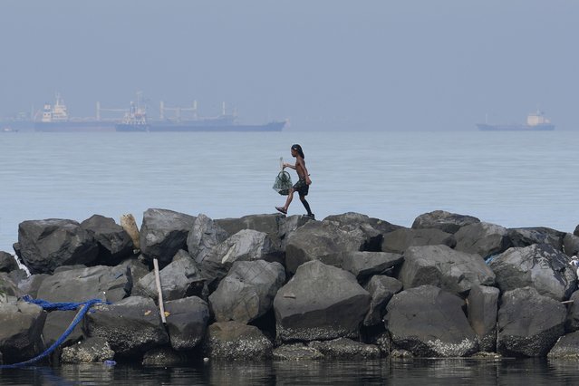 A boy holds his day's catch of crabs as he walks along the breakwater in Manila, Philippines on Saturday, September 25, 2021. (Photo by Aaron Favila/AP Photo)