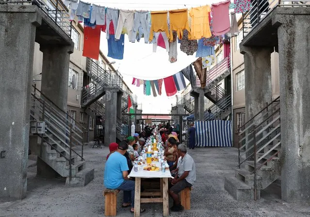 People sit at a long makeshift table before an Iftar, breaking of the fast, during the holy month of Ramadan in Heideveld on the Cape Flats, Cape Town, South Africa, on March 30, 2024. (Photo by Esa Alexander/Reuters)