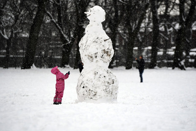 A child looks at a giant snowman as they stand in a snow-covered Victoria Park in Glasgow on February 9, 2021. Cold weather swept across northern Europe bring snow and ice. (Photo by Andy Buchanan/AFP Photo)
