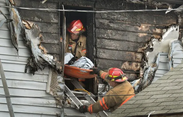 Syracuse firefighters remove a body through an upstairs window at the scene of a fatal fire Friday May 6, 2016 in Syracuse, N.Y. The blaze was reported early Friday morning.  When firefighters arrived just minutes after receiving a 911 call, the front of the house was engulfed in flames, officials said. (Photo by David Lassman/The Syracuse Newspapers via AP Photo)