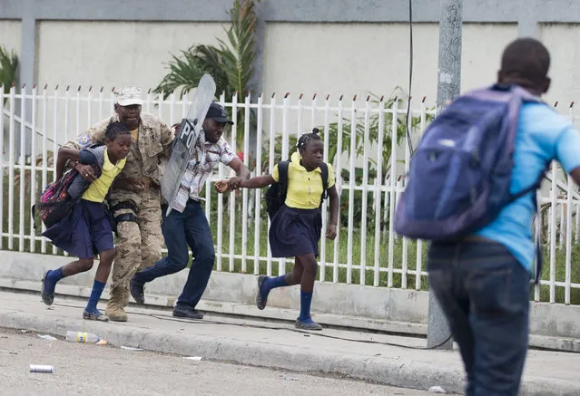 A police officer helps a man and two students as they run away from tear gas and violence during a protest against the ratification of interim Prime Minister Jean Michel Lapin, in front of the Parliament building in Port-au-Prince, Haiti, Thursday, May 30, 2019. (Photo by Dieu Nalio Chery/AP Photo)