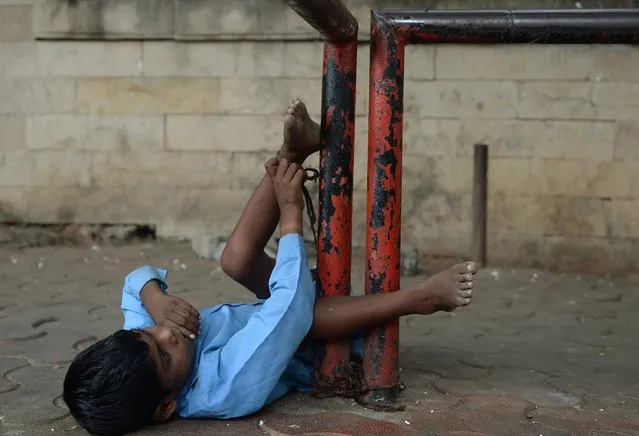 In this photograph taken on May 20, 2014 nine year old Indian boy Lakhan Kale is tied with a cloth rope around his ankle, to a bus-stop pole in Mumbai.(Photo by Punit Paranjpe/AFP Photo)