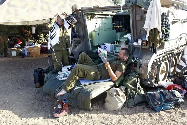 An Israeli soldier reads a newspaper as another one prepares to pray next to an armoured personnel carrier (APC) outside the southern Gaza Strip July 17, 2014. Palestinians rushed to shops and banks on Thursday as a five-hour humanitarian truce agreed by Israel and Hamas came into force, hours after the Israeli military said it had fought off gunmen who infiltrated from Gaza. About a dozen Palestinian fighters tunnelled under the border, emerging near an Israeli community. (Photo by Ronen Zvulun/Reuters)