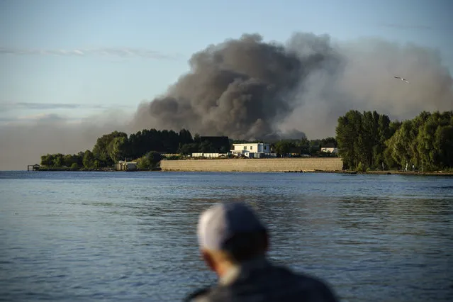 A fisherman watches smoke rise after Russian forces launched a missile attack on a military unit in the Vyshhorod district on the outskirts of Kyiv, Ukraine, Thursday, July 28, 2022. (Photo by David Goldman/AP Photo)