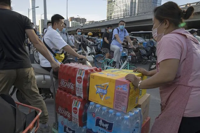 Cyclists past by workers delivering beverage near a mall on the streets of Beijing Tuesday, May 19, 2020. As job losses surge, China is joining the United States and other governments in rolling out stimulus spending to revive its virus-battered economy. Companies and the public are looking to the meeting of the ceremonial national legislature starting Friday, May 22, 2020 for details. One closely watched indicator: Whether Beijing skips for the first time setting an economic growth target in a sign of how uncertain even the rest of this year is. (Photo by Ng Han Guan/AP Photo)