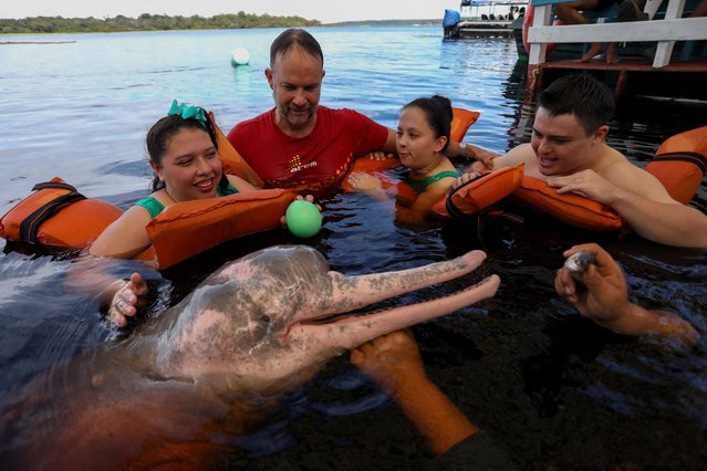 Physiotherapist Igor Simoes Andrade and young people with disabilities swim with pink dolphins (Inia geoffrensis) on the Rio Negro river in Iranduba, Amazonas state, Brazil, on February 20, 2025. Physiotherapist Igor Simoes Andrade launched the “Bototheraty” program in 2016, which provides sessions for people with physical and mental disabilities by taking them to swim with wild pink freshwater dolphins in the Amazon. (Photo by Michael Dantas/AFP Photo)